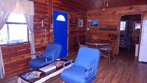 L’intérieur d’un chalet accueillant, avec des murs en bois, un coin repas comprenant une table et des chaises, et une porte bleue.