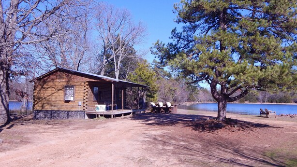 Un chalet rustique doté d’une véranda et de meubles d’extérieur, entouré d’arbres et bordé par un lac.