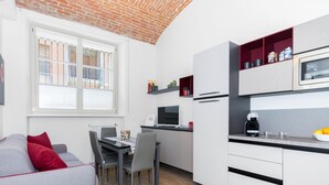 A modern kitchen with white cabinets, a microwave, and a coffee machine. There is a dining table with chairs and a red cushion. - Loft del Conte nei Pressi Della Mole by Wonderful Italy (Turin)