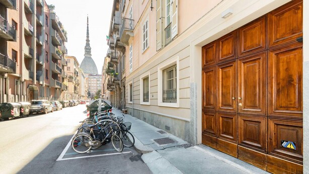 A street with parked bicycles, a large wooden door, and a building with balconies. - Loft del Conte nei Pressi Della Mole by Wonderful Italy (Turin)