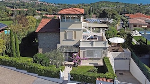 Ein zweigeschossiges Haus mit rotem Ziegeldach, einem Balkon mit Liegestühlen und Blick auf das Meer.