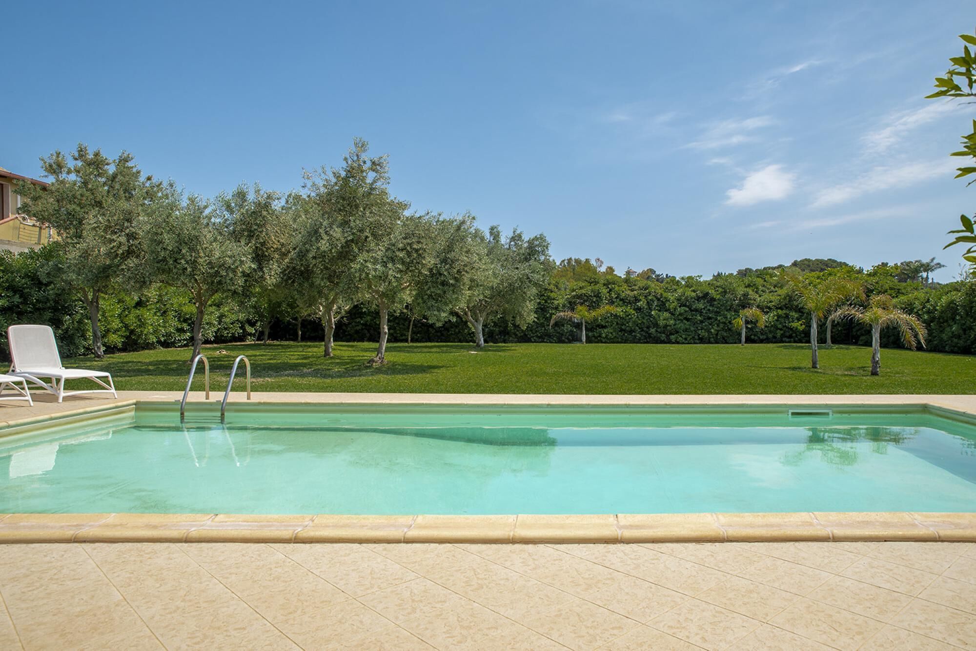 A rectangular swimming pool with a tiled deck, surrounded by a well-maintained lawn and trees.