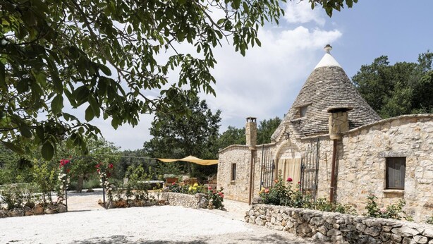 A stone building with a conical roof, surrounded by a garden with various plants and flowers. - Trullo Fragno by Wonderful Italy (Noci)
