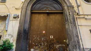 Une grande porte en bois à arc surmontée d’un balcon en métal.