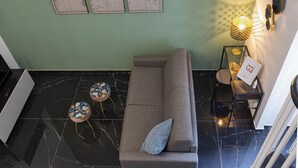 Uma sala de estar moderna com um sofá cinzento, duas mesas redondas e uma luminária fixada na parede.