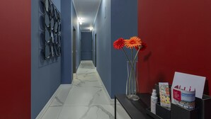 Corredor com paredes azuis, piso de mármore e um balcão de recepção preto, com um vaso de flores e folhetos.