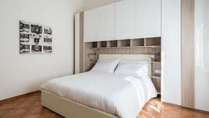 Quarto com cama, cabeceira com prateleiras embutidas e colagem de fotos na parede.