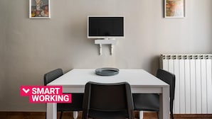 Quarto moderno com uma mesa branca, cadeiras pretas, uma TV e duas imagens emolduradas nas paredes.