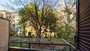 Varanda com guarda-corrimão de metal, vista para um jardim com árvores e uma pequena construção de madeira.