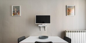 A modern room with a white table, black chairs, a TV, and two framed pictures on the walls. - Appartamento nel Verde in Saffi by Wonderful Italy (Bologna)