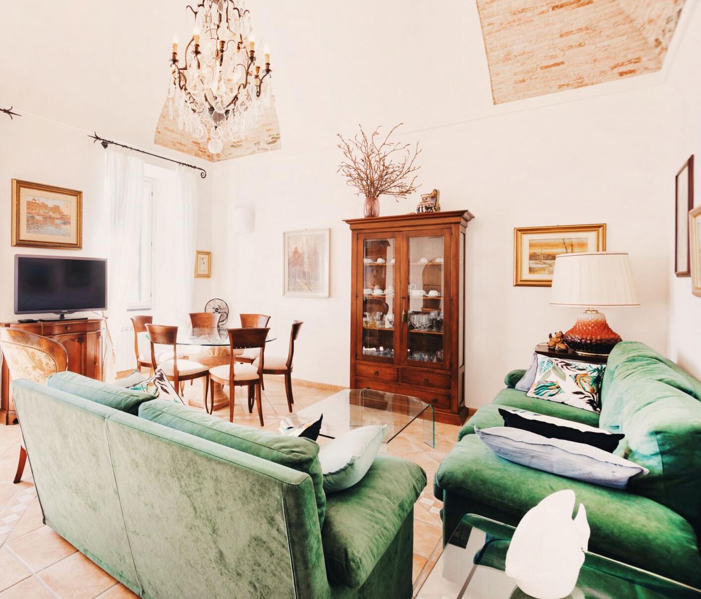 A living room with green sofas, a wooden cabinet, a chandelier, and a television.