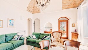 A spacious living room with a green sofa set, a wooden chair, and a glass coffee table.