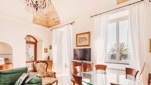 A living room with a green sofa, a wooden armchair, a glass dining table, and a TV.