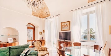 Una sala de estar con un sofá verde, un sillón de madera, una mesa de comedor de cristal y un televisor.
