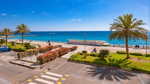 A coastal promenade with a clear view of the sea, palm trees, and a pedestrian path.