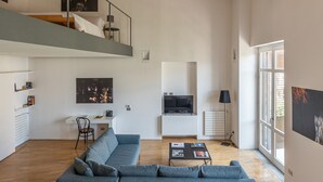 A spacious living room with a large gray sectional sofa, a flat-screen TV mounted on a white cabinet, and a staircase leading to an upper level. - Cala Loft by Wonderful Italy (Palermo)
