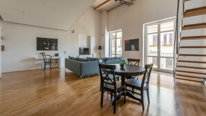 A spacious living area with a wooden floor, a dining table with chairs, a grey sofa, and a TV mounted on the wall. - Cala Loft by Wonderful Italy (Palermo)