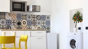 A compact kitchen with a microwave, a washing machine, and a dining area with yellow chairs. - Casa Mil by Wonderful Italy (Naples)