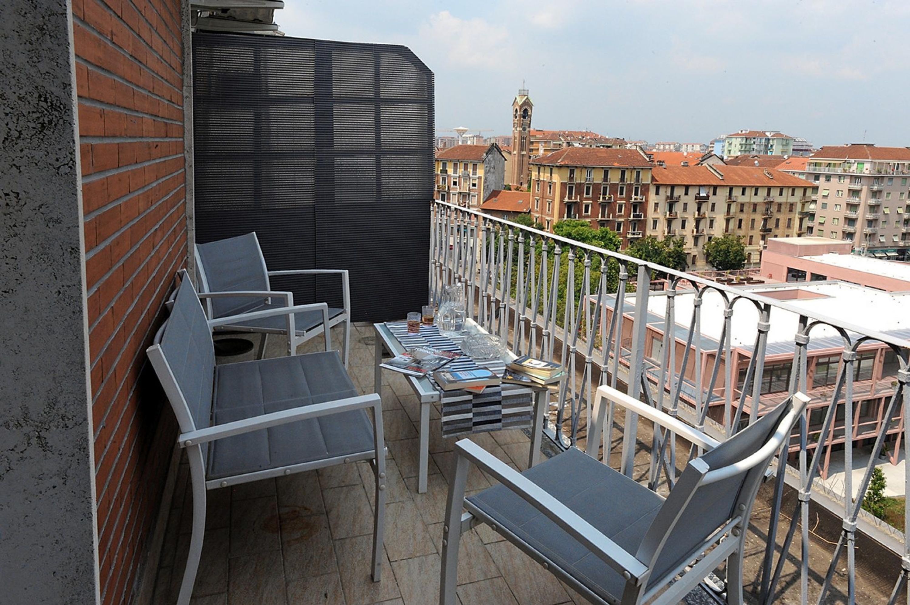 Un balcone con due sedie e un tavolo, affaccia su una città con edifici e una torre.