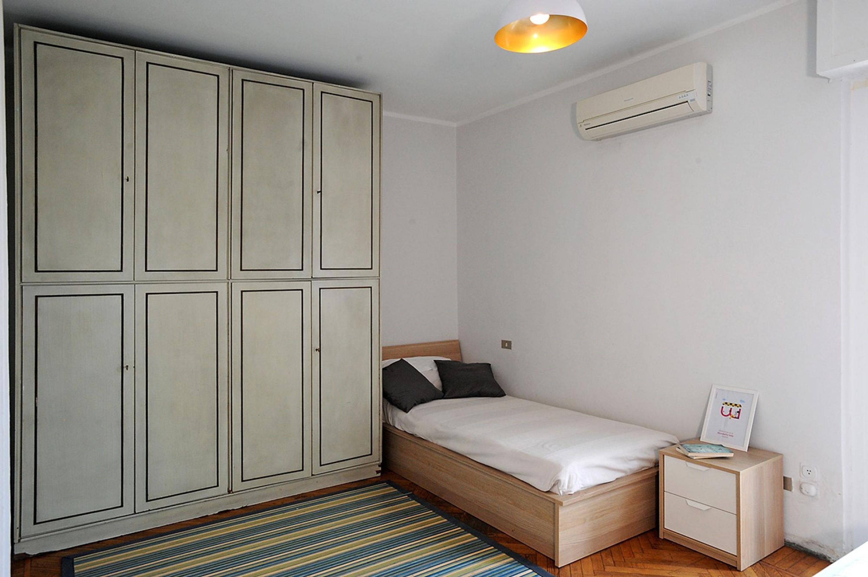 A bedroom with a single bed, a nightstand, a wardrobe, and a ceiling light.