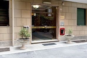 Entrada de un edificio con puerta de vidrio, dos macetas, un buzón rojo y un letrero de mostrador de viajes.