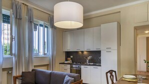 A compact kitchen with white cabinets, a dining table with chairs, and a hanging light fixture.