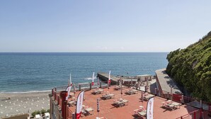 A rooftop terrace with tables and chairs, overlooking the sea and a beach.