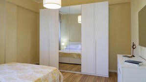 A bedroom with a bed, a wardrobe, a desk with a lamp, and a mirror.