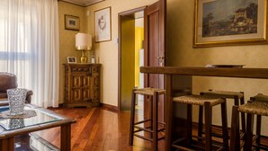 A room with wooden flooring, a glass coffee table, a sofa, a cabinet, a lamp, a painting, and a door leading to another room. - Fossalta Vintage Apartment by Wonderful Italy (Bologna)