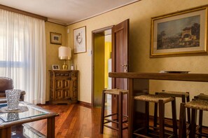 A room with wooden flooring, a glass coffee table, a sofa, a cabinet, a lamp, a painting, and a door leading to another room. - Fossalta Vintage Apartment by Wonderful Italy (Bologna)