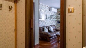 A room with a brown leather sofa, wooden flooring, and floral wallpaper. - Fossalta Vintage Apartment by Wonderful Italy (Bologna)