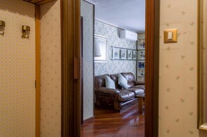 A room with a brown leather sofa, wooden flooring, and floral wallpaper. - Fossalta Vintage Apartment by Wonderful Italy (Bologna)