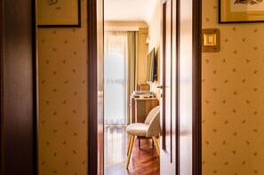 A hallway with patterned wallpaper, a chair, a desk with a computer, and a mirror on the wall.
