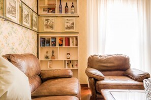 Ein Wohnzimmer mit zwei Ledersesseln, einem Bücherregal mit Büchern und Dekoartikeln sowie einem floralen Wandmuster.