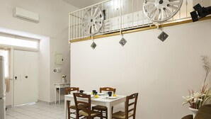 Uma área de refeições com uma mesa branca, quatro cadeiras de madeira e um sofá marrom.