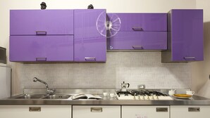 Uma cozinha com armários roxos, uma pia de aço inoxidável e um fogão a gás.