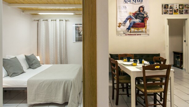 Um quarto com uma cama, uma mesa de jantar com cadeiras e um cartaz na parede.