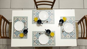 Uma mesa de jantar posta com pratos, xícaras e uma tigela, rodeada por cadeiras.