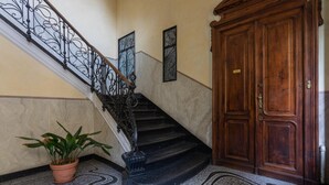 Uma escadaria de mármore com guarda-corpos de metal preto, um vaso de planta e uma porta de madeira.