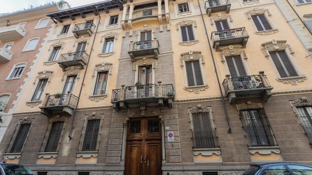 Um edifício com vários andares, entrada central, varandas e placa de proibido estacionar.