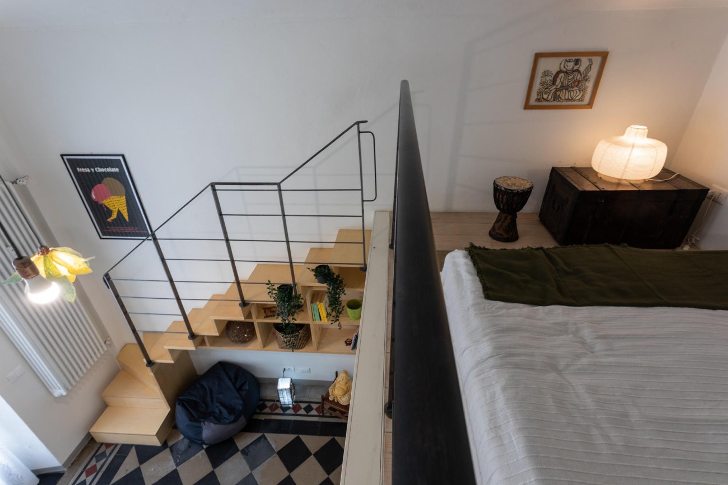 A bedroom with a bed, a staircase, and a nightstand with a lamp.