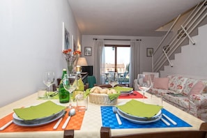 Un coin repas avec une table dressée pour deux personnes, un escalier et un canapé en arrière-plan.