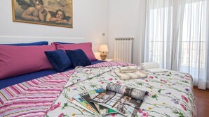 Une chambre à coucher avec un lit, des oreillers, une lampe, un radiateur et une fenêtre avec des rideaux.