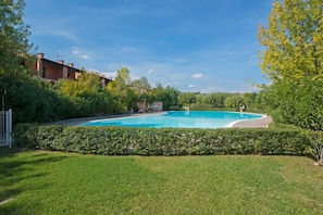 A swimming pool surrounded by well-maintained grass and hedges, with buildings in the background. - Residence Edera 18 by Wonderful Italy (Polpenazze del Garda)