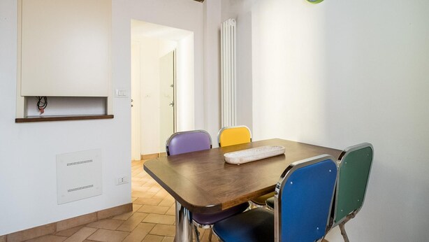 Une pièce avec une table en bois, deux chaises, une horloge au mur et un radiateur.