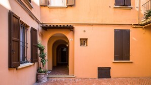 Une ruelle étroite, avec un sol carrelé, une plante en pot et une porte donnant sur un intérieur sombre.
