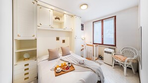 A bedroom with a bed, bedside tables, a radiator, a window, and a chair. - Residence Giardino 3 by Wonderful Italy (Soiano del Lago)