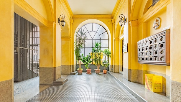 A hallway with yellow walls, a tiled floor, and potted plants. - A Due Passi Dalla Mole by Wonderful Italy (Turin)