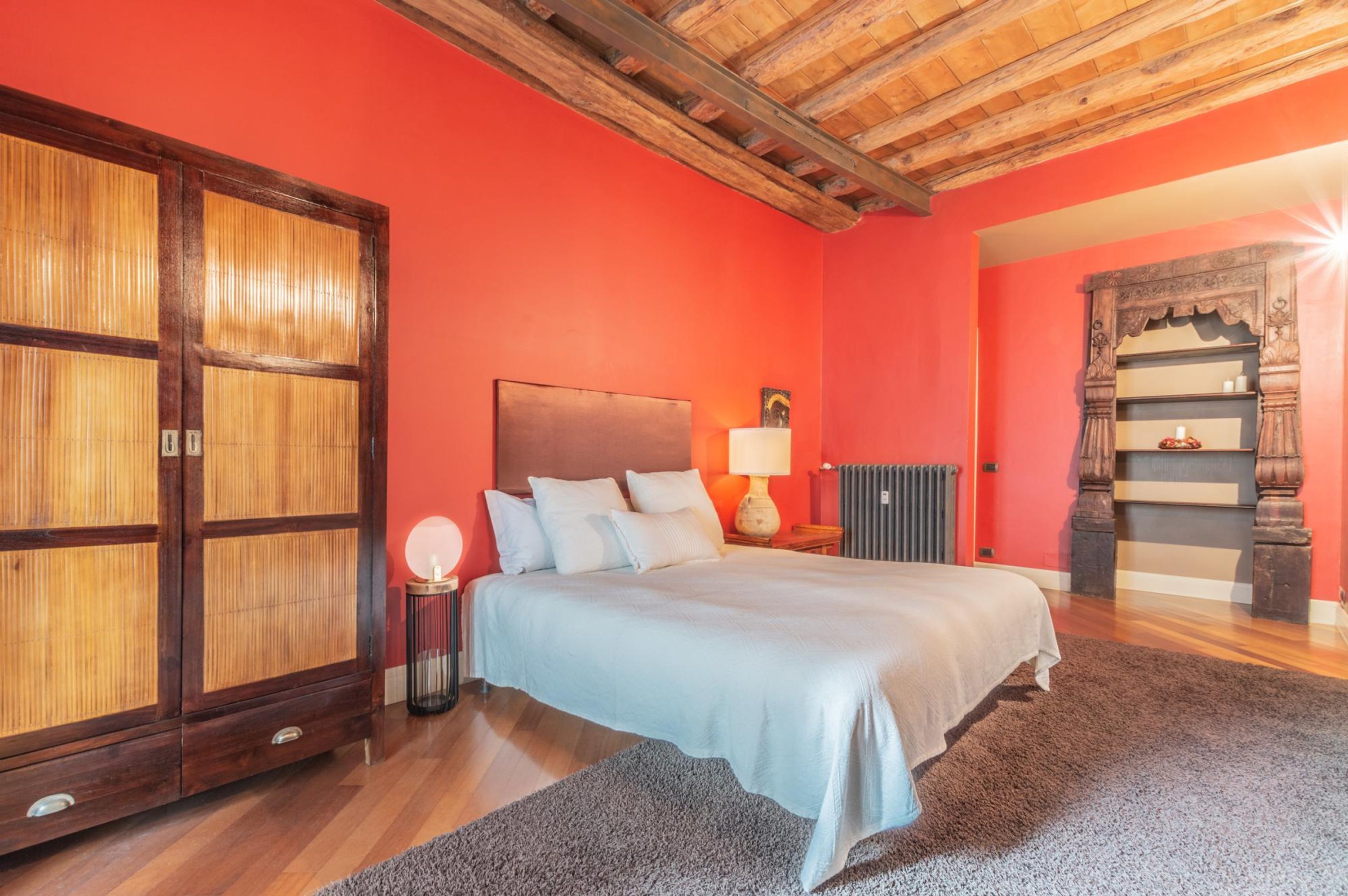 A bedroom with a large bed, wooden wardrobe, and a red wall.
