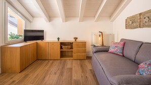 A cozy living room with a wooden desk, a television, a grey sofa with colorful cushions, and a radiator. - Le Niche Holiday Home - Terrace by Wonderful Italy (Palermo)